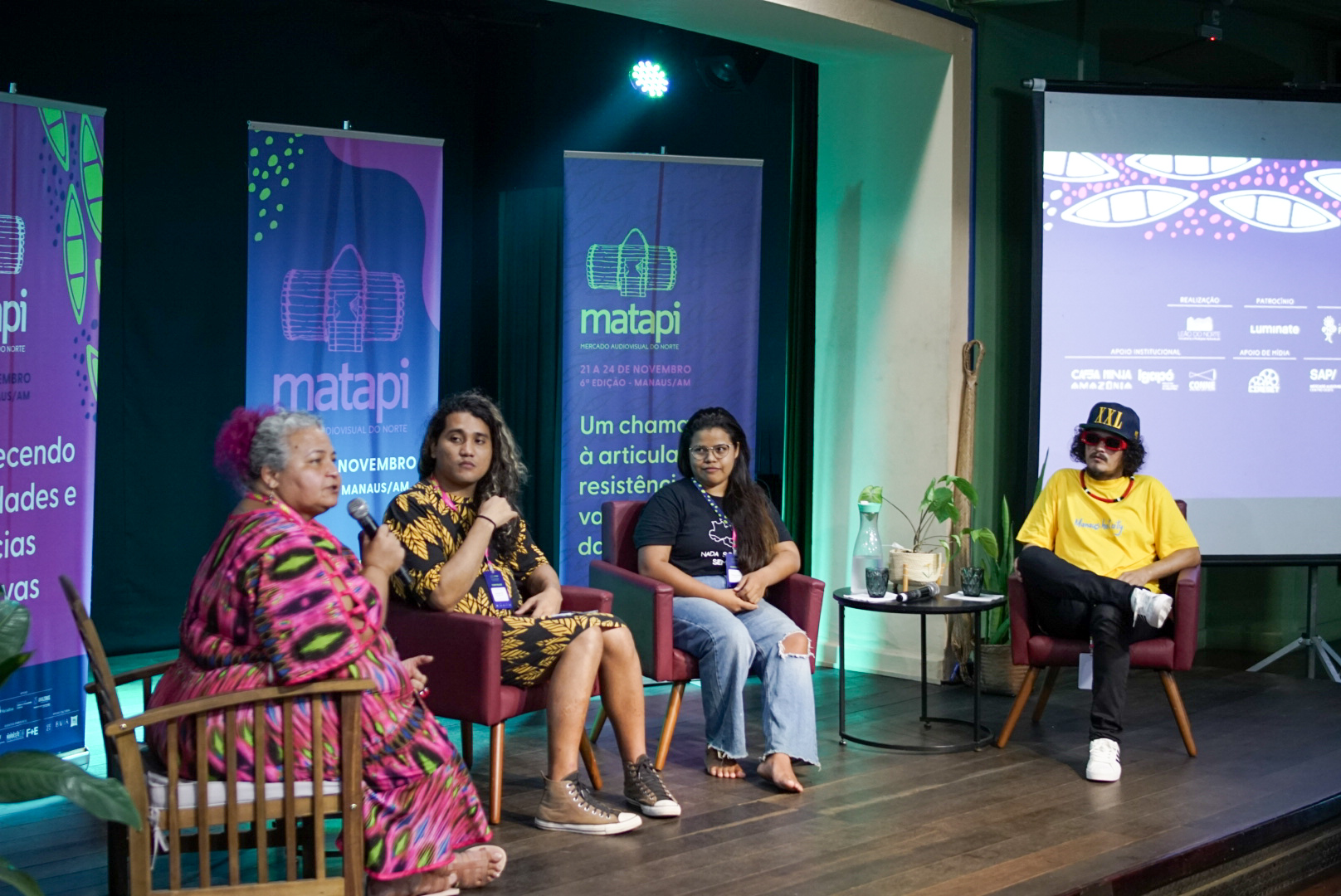 Matapi 2023: dupla conversa no palco, diante dos banners da 6ª edição
