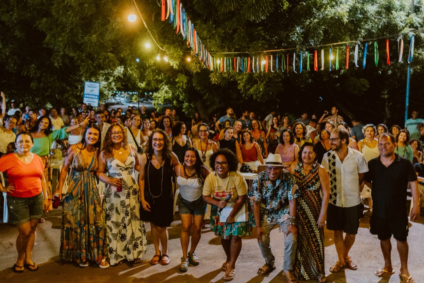 Climate Story Lab 2025: roda de pessoas sorrindo ao ar livre, sob bandeirinhas coloridas